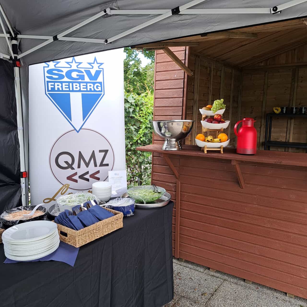 Frische Salate, das QMZ-Logo und eine einladende Bar - Ihre VIP-Catering-Oase.